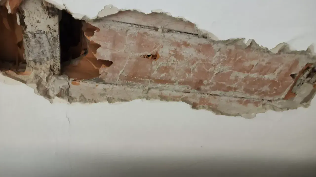 Intonaco danneggiato rivela l'intradosso del solaio con mattoni a vista e travi in legno.