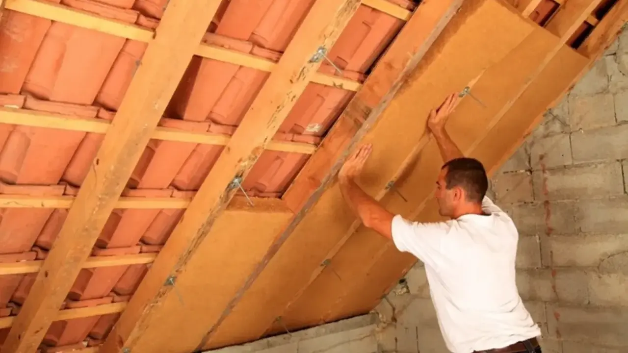 Operaio posiziona pannelli per isolamento soffitto interno, tra travi in legno e tegole.