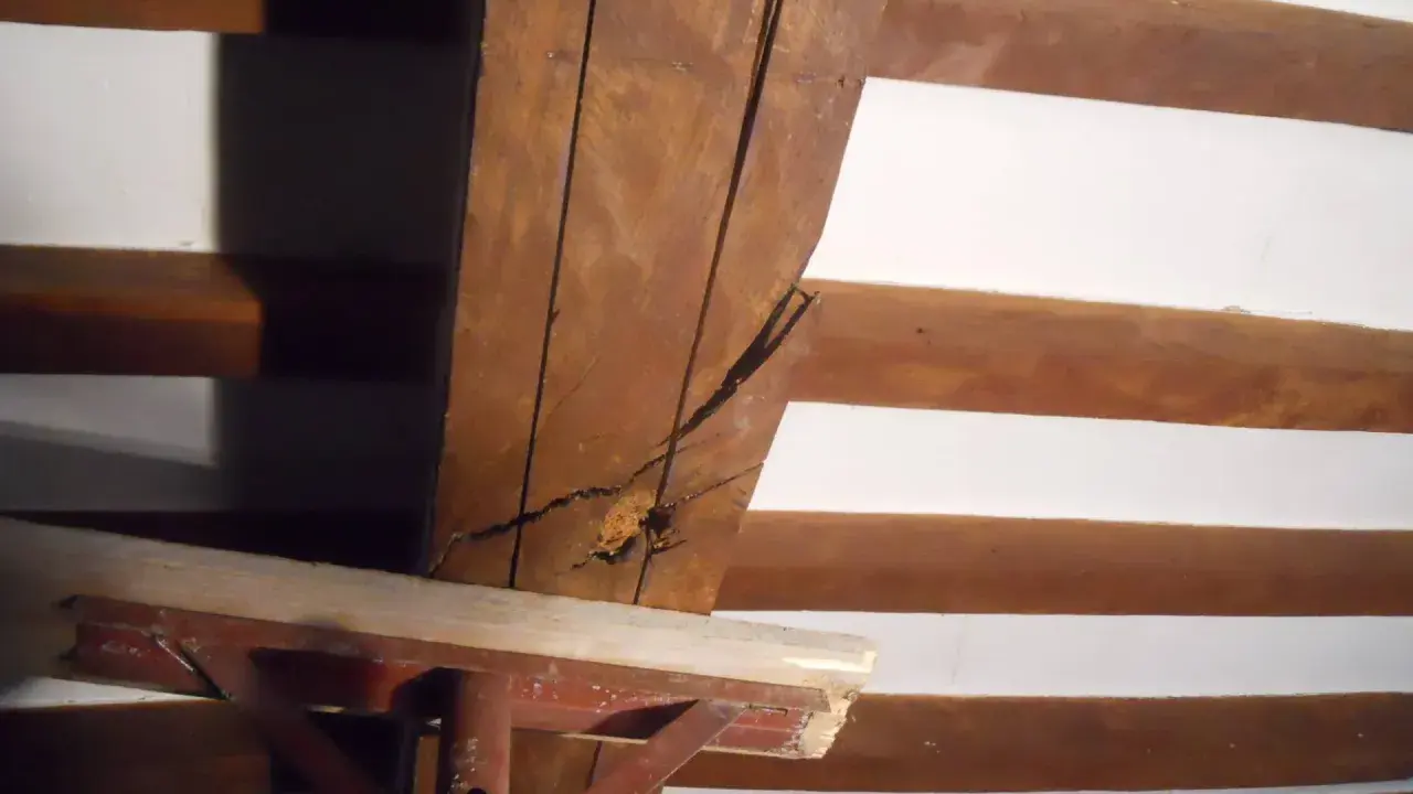 Dettaglio di travi in legno con crepe, in attesa di consolidamento. Supporto metallico provvisorio.