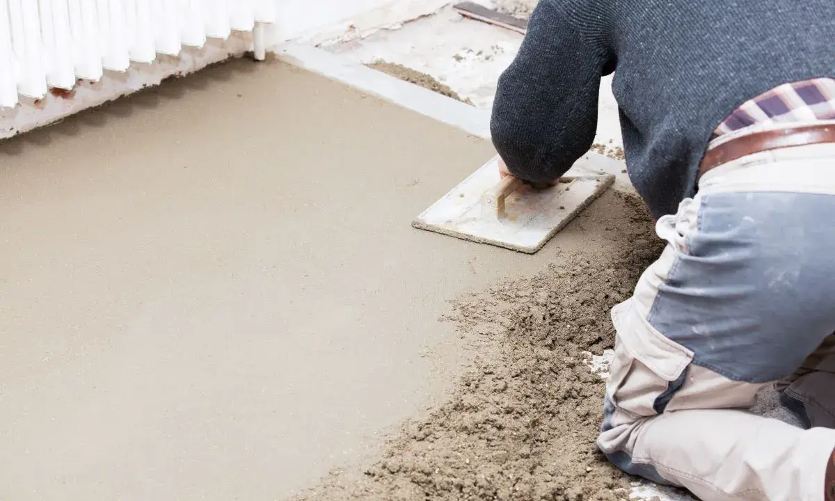 Operaio stende il massetto con una spatola, mostrando la differenza tra massetto e calcestruzzo grezzo.