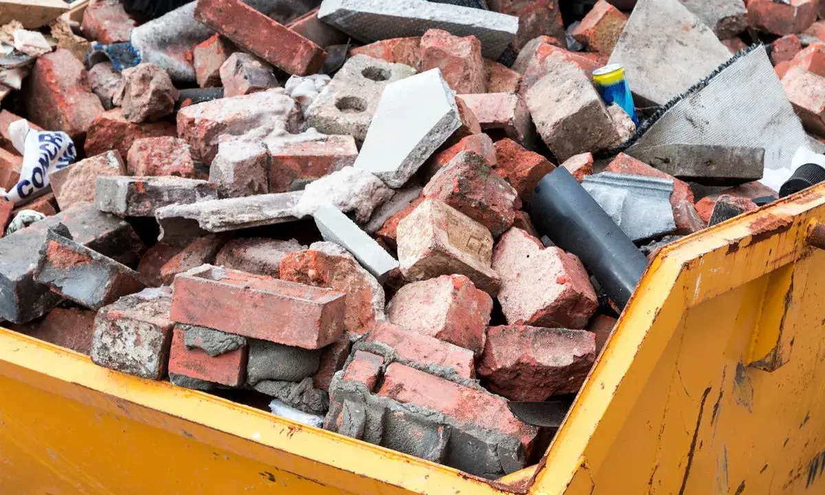 Cumulo di mattoni rotti e detriti edili in un cassone giallo. Questo è il materiale di risulta, scarti di demolizione pronti per lo smaltimento.