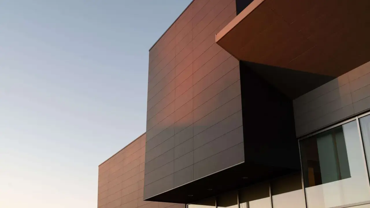 Edificio moderno con facciata ventilata in pannelli scuri e color rame, illuminato dalla luce del tramonto.