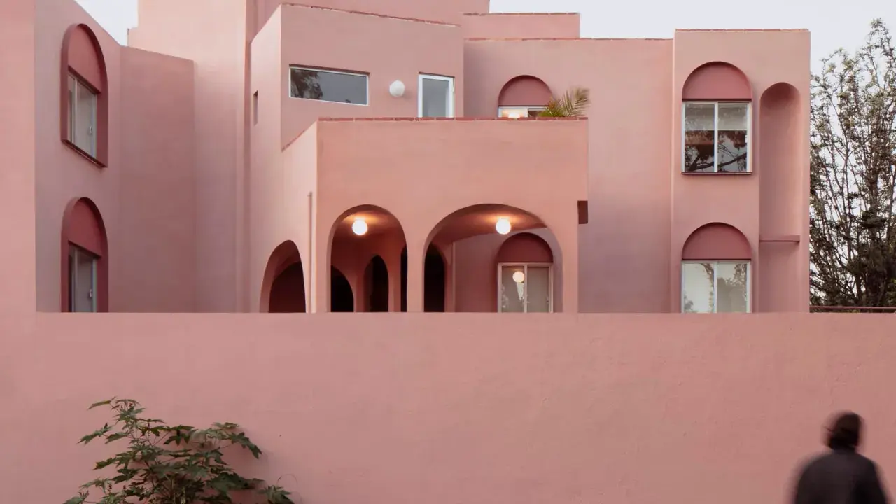 Edificio moderno con un particolare colore intonaco esterno rosa cipria. Archi e finestre a tutto sesto creano un gioco di luci e ombre.
