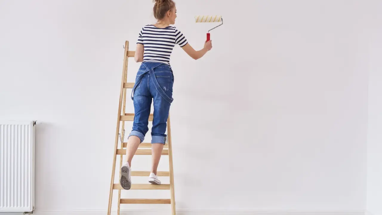 Donna su scala con rullo, pronta a tinteggiare le pareti di bianco.