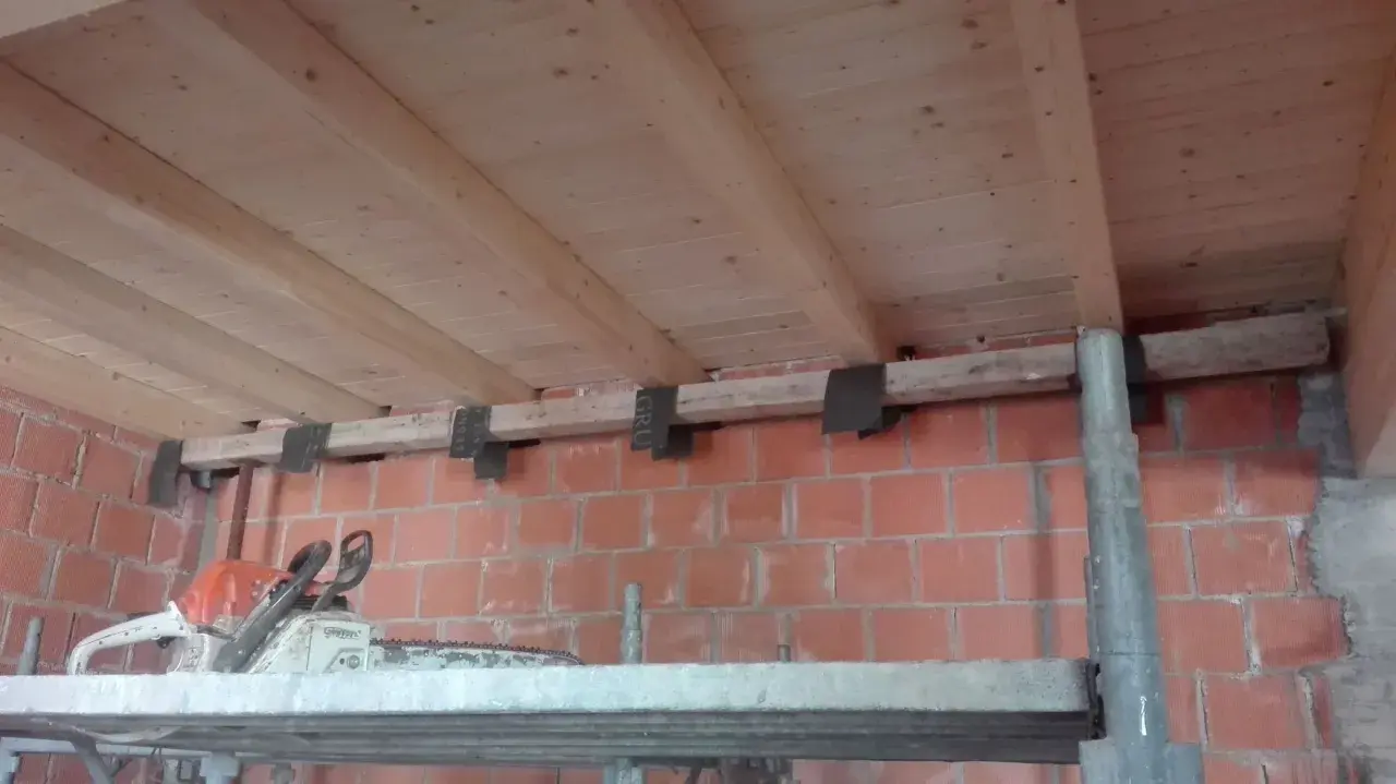 Travetti in legno per solaio, con staffe metalliche fissate a un muro di mattoni. L'interasse travetti solaio è visibile.