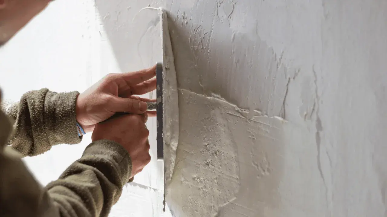 Mani esperte creano una finitura a frattazzo su un muro grezzo, dando forma alla texture.