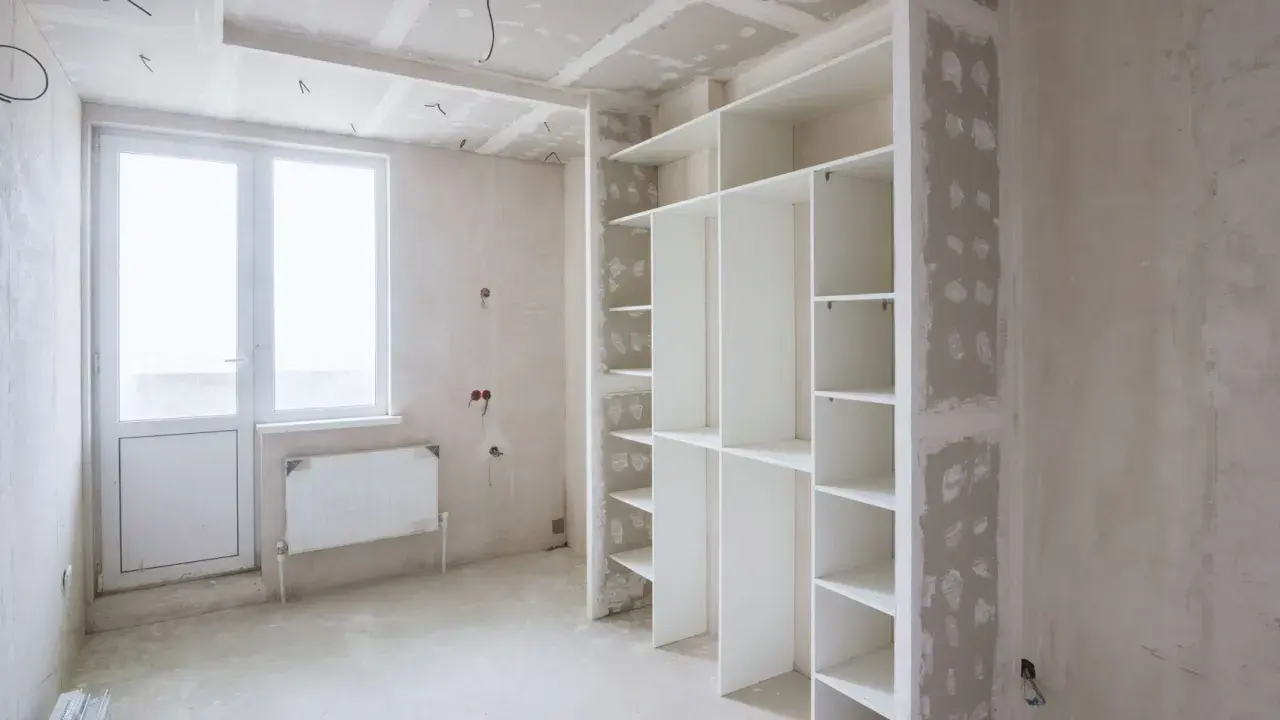 Un armadio bianco con ripiani è in fase di installazione. Sopra l'armadio, si intravede il cartongesso del soffitto, in attesa di finitura.