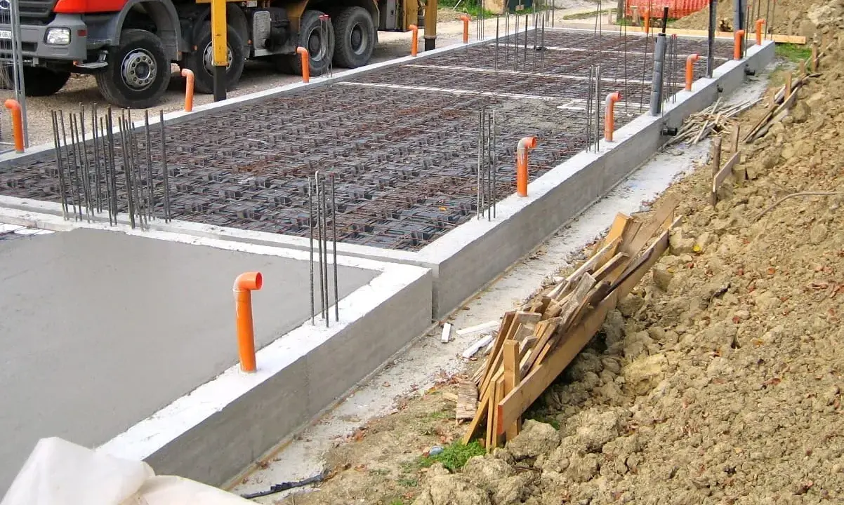 Costruzione in corso: rete di armatura e tubi arancioni per l'aerazione vespaio. Cemento fresco e un camion Beton.