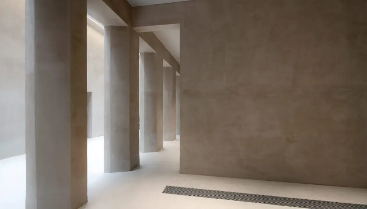 Colonnato moderno con pareti e pilastri in intonaco o stucco color sabbia, illuminato da luce soffusa.
