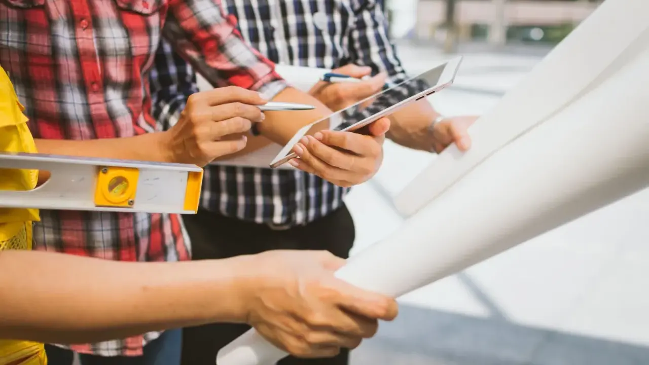Team di operai esamina progetto su tablet, livella e rotoli di carta. Aggiornamento sal stato avanzamento lavori.