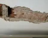 Intonaco danneggiato rivela l'intradosso del solaio con mattoni a vista e travi in legno.