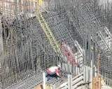 Operaio lavora su un'impalcatura di ferro per il cemento armato. La sua presenza suggerisce la cura necessaria per garantire la durata del cemento armato.
