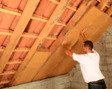 Operaio posiziona pannelli per isolamento soffitto interno, tra travi in legno e tegole.