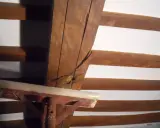 Dettaglio di travi in legno con crepe, in attesa di consolidamento. Supporto metallico provvisorio.