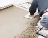 Operaio stende il massetto con una spatola, mostrando la differenza tra massetto e calcestruzzo grezzo.