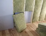 Pannelli di lana di roccia pronti per l'isolamento termico casa, inseriti tra le travi di legno di una parete in costruzione.