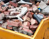 Cumulo di mattoni rotti e detriti edili in un cassone giallo. Questo è il materiale di risulta, scarti di demolizione pronti per lo smaltimento.
