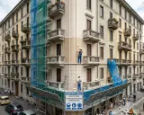 Lavoratori in azione per dipingere casa esterno, con impalcature e teli blu che coprono la facciata in ristrutturazione.