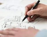 Mano che disegna dettagli architettonici su carta, con un pennarello nero. Si intravedono annotazioni come "LED STRIP", in linea con l'art. 34 bis DPR 380/01.