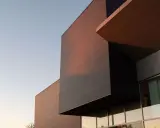 Edificio moderno con facciata ventilata in pannelli scuri e color rame, illuminato dalla luce del tramonto.