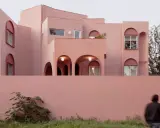 Edificio moderno con un particolare colore intonaco esterno rosa cipria. Archi e finestre a tutto sesto creano un gioco di luci e ombre.