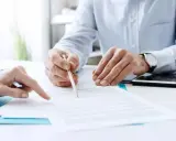 Due mani esaminano un documento, una indica un punto mentre l'altra tiene una matita, forse per la dichiarazione di inizio attività.