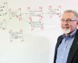 Uomo spiega il diagramma del **critical path method** per la costruzione di un serbatoio, con attività e durate.