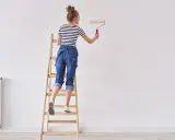 Donna su scala con rullo, pronta a tinteggiare le pareti di bianco.