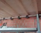 Travetti in legno per solaio, con staffe metalliche fissate a un muro di mattoni. L'interasse travetti solaio è visibile.