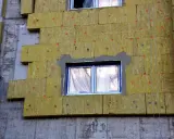 Iniziano i lavori per fare il cappotto alla casa: pannelli isolanti gialli fissati al muro grezzo, con finestre protette.