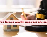 Modello di casa, martelletto da giudice e testo "Cosa fare se erediti una casa abusiva". Guida su come sanare un abuso edilizio ereditato.