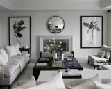 Soggiorno elegante con divani chiari, camino, specchio rotondo e opere d'arte botaniche. La finitura pareti interne è liscia e bianca, esaltando l'arredamento.