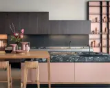 Cucine moderne con un mix di colori audaci: ante rosa cipria, top in marmo scuro e scaffalature color rame.