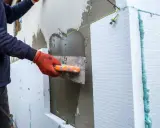 Lavoratore applica intonaco su pannelli isolanti per creare una parete a cappotto.