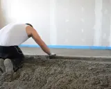 Operaio al lavoro per stendere il massetto edilizia, creando una base solida per il pavimento.
