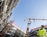 Operaio con giubbotto alta visibilità osserva un cantiere edile con gru e impalcature. Capire cassa edile come funziona è fondamentale per la sicurezza.