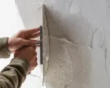 Mani esperte creano una finitura a frattazzo su un muro grezzo, dando forma alla texture.