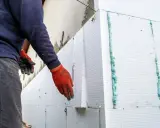 Installazione di un cappotto termico su intonaco esistente. Pannelli in polistirene espanso vengono fissati con schiuma espansa.