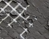 Rete in fibra di vetro coperta da malta grigia, un dettaglio di un intervento locale per rinforzare una superficie.