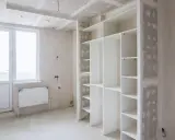 Un armadio bianco con ripiani è in fase di installazione. Sopra l'armadio, si intravede il cartongesso del soffitto, in attesa di finitura.