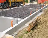 Costruzione in corso: rete di armatura e tubi arancioni per l'aerazione vespaio. Cemento fresco e un camion Beton.