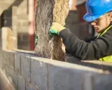 Operaio con casco blu installa isolante, valutando i cappotto termico svantaggi.