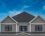 La facciata di una casa moderna con un elegante colore esterno casa tortora scuro, finestre nere e un tetto scuro sotto un cielo blu intenso.