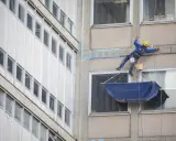 Operaio in corda esegue consolidamenti strutturali su un edificio, con attrezzature di sicurezza e secchi.