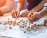 Mani che studiano una mappa con modelli di edifici, per capire cosa sono gli standard urbanistici e come definire lo sviluppo di una città.
