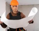 Un esperto capomastro, con casco arancione, studia attentamente un progetto, dimostrando il vero significato di guida e competenza in cantiere.
