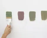 Pennello con vernici ecologiche in diverse tonalità di verde e un tocco di malva su sfondo bianco.