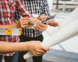 Team di operai esamina progetto su tablet, livella e rotoli di carta. Aggiornamento sal stato avanzamento lavori.