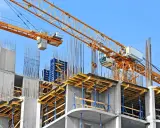 Cantiere edile con gru gialla e strutture in cemento armato. Si nota il puntellamento solaio con supporti blu e tavole di legno.