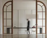 Archi interni casa con porte in legno che incorniciano una cucina moderna. Una figura sfocata attraversa lo spazio.